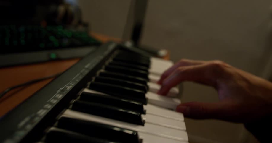 Man sits playing on keyboard set on table near computer and music interface