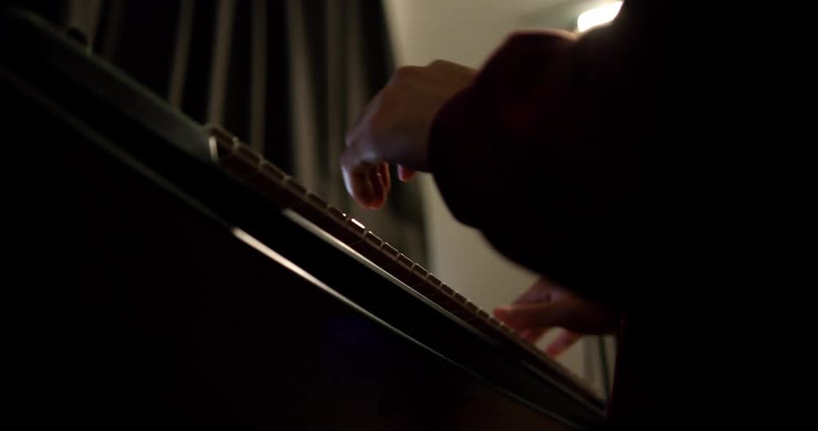 Man with beard wearing baseball cap plays piano near curtained windows