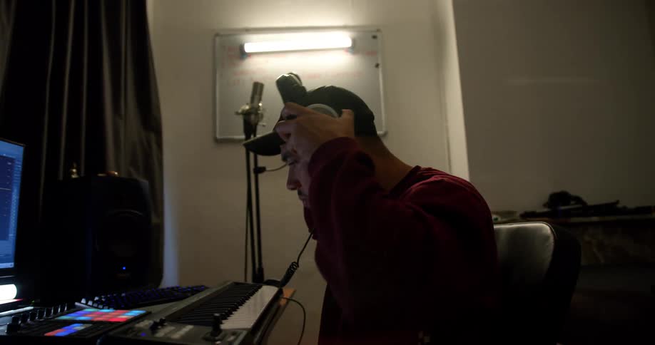 A man sitting in front of a keyboard and computer puts his headphones on as he moves to music