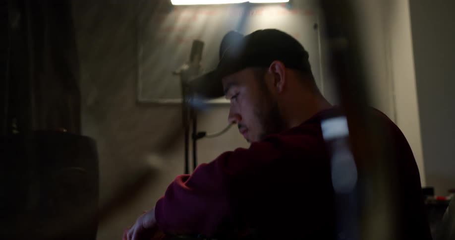 A man with a hat sitting at a desk making music on a computer