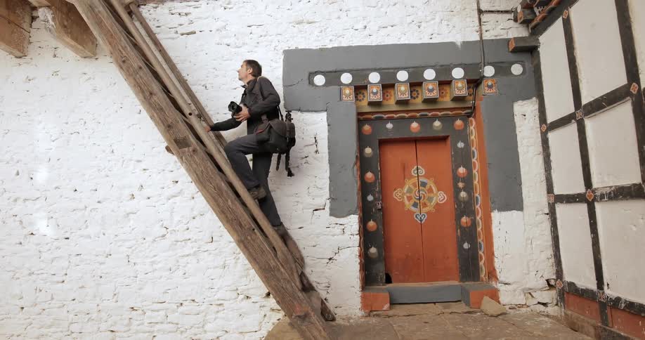 A man carrying a camera climbs some stairs on the side of a building