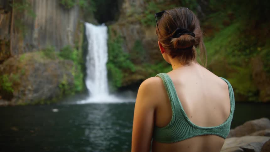Woman in a biking watches the waterfall near the lake