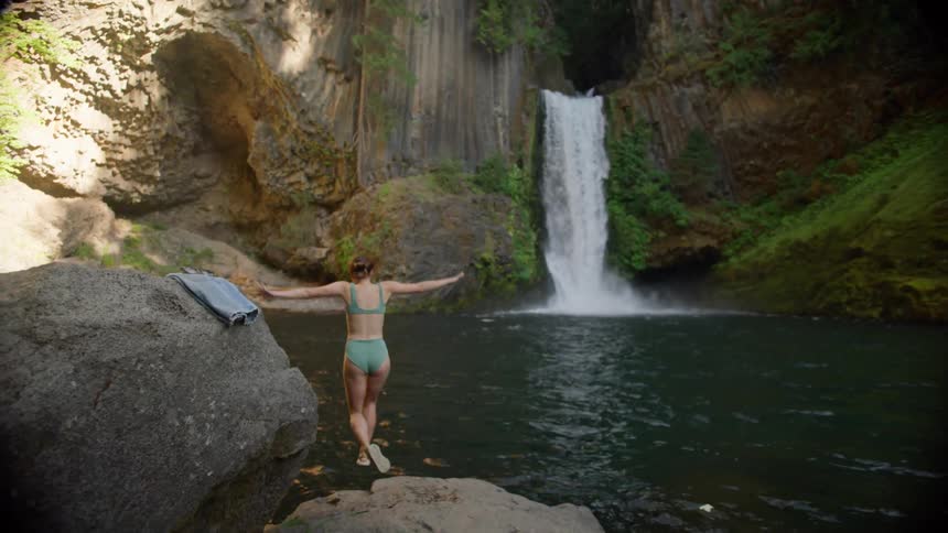 A teenage girl jumps off of a rock and in to the water