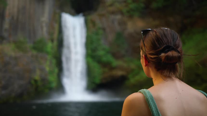Woman with sunglasses and a green bikini watches the waterfall