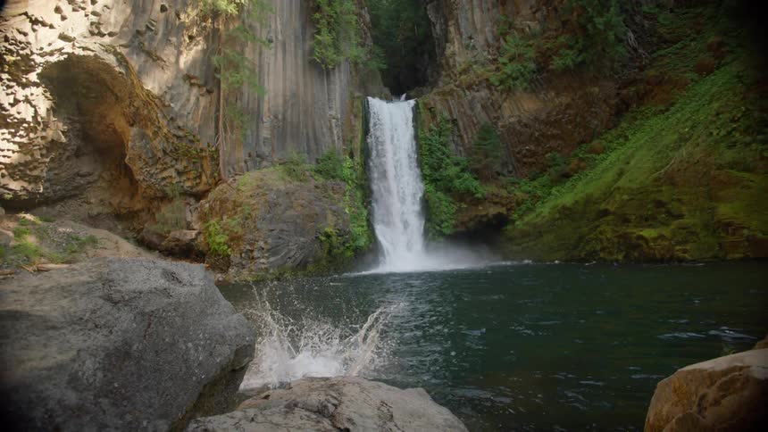Young shirtless man dives from a rock into a river near a waterfall
