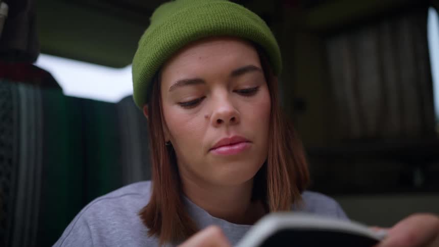 Woman with a green beanie and brown hair writes in a notebook in a vehicle