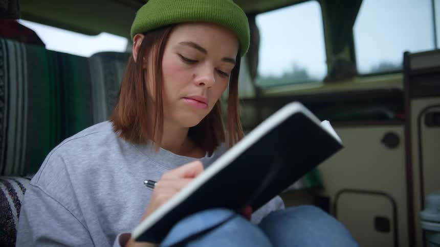 A woman is sitting down and writing in a journal