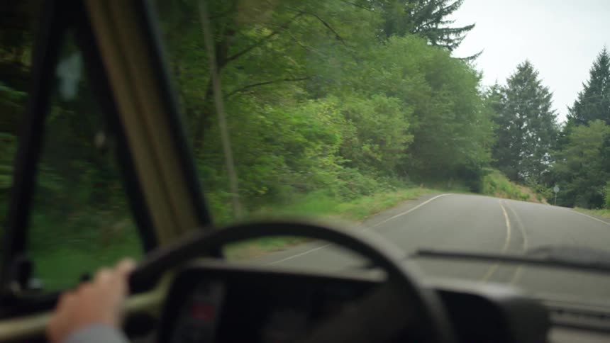 A young woman drives a car along a road through a woodland during the day