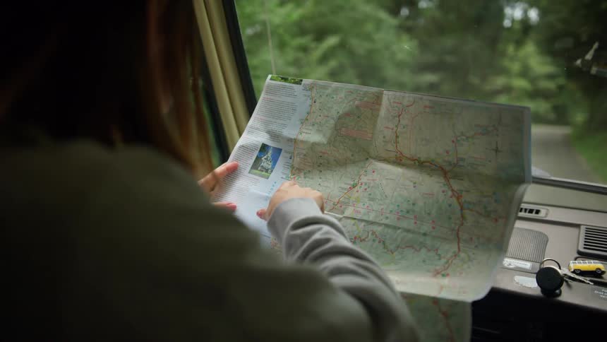 A woman in a vehicle holding a map with a road and trees in the background