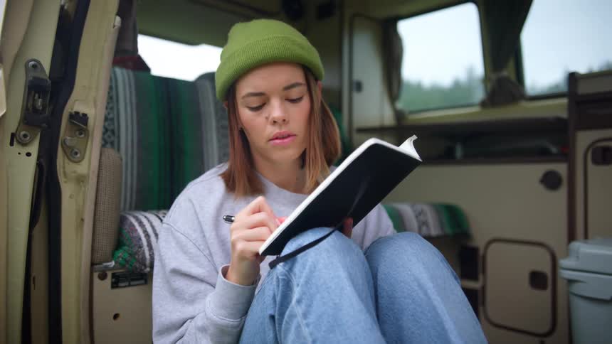Young woman sits inside camper writing in journal