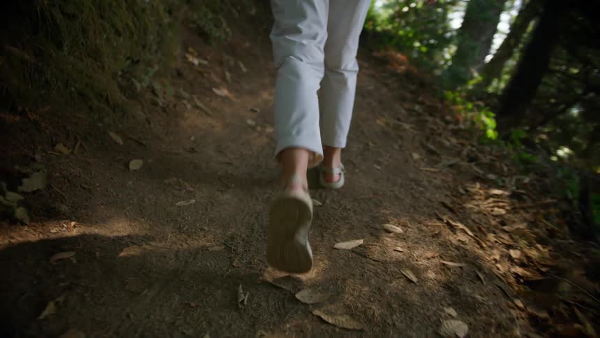 Womans legs with pants and sandals walks on forest track