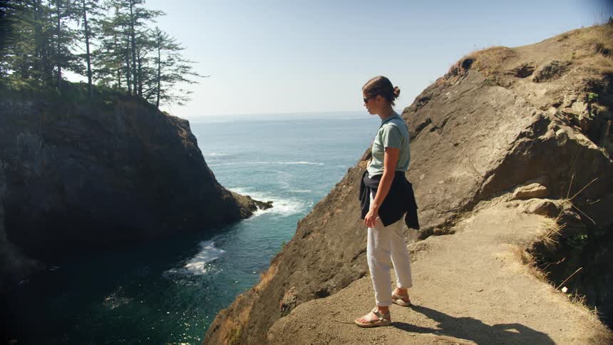 A woman stands on a cliff by the ocean