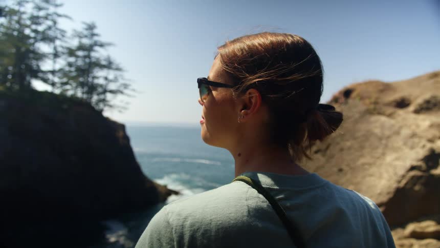 A woman stops on a hike along a cliff overlooking the ocean