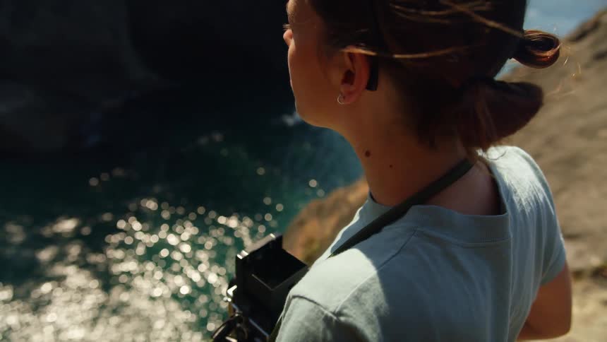 A woman holds a camera near the cliff