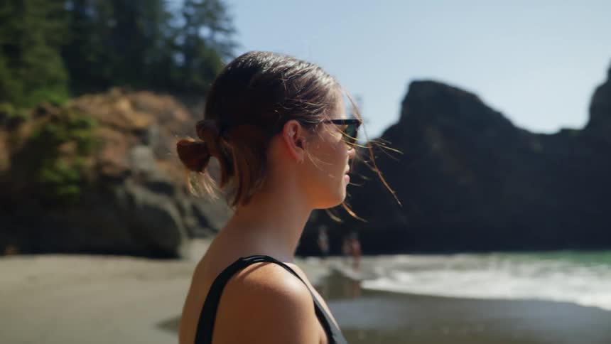 Woman with glasses and a black swimsuit stands on the beach and goes swimming