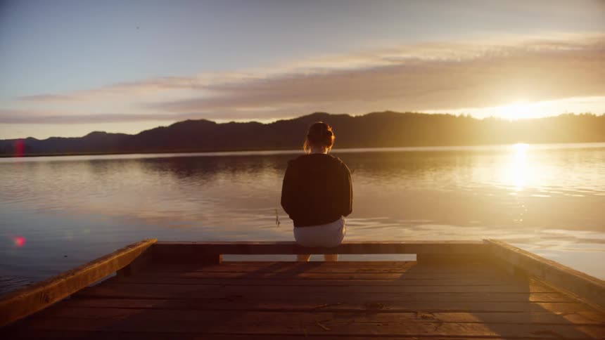 A woman sits on the dock as the sun sets