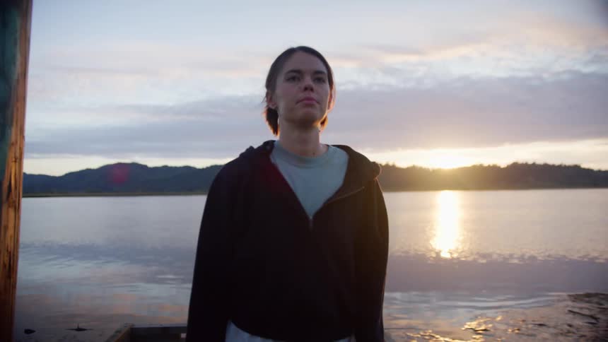 A woman walking near the coast with water land the sky and clouds in the background