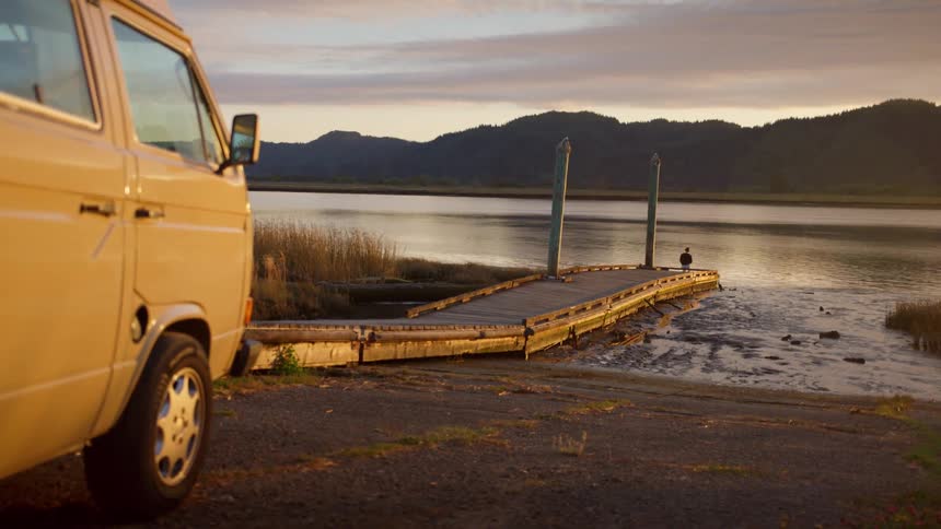 A white van is parked next to a pier along the coast of a lake