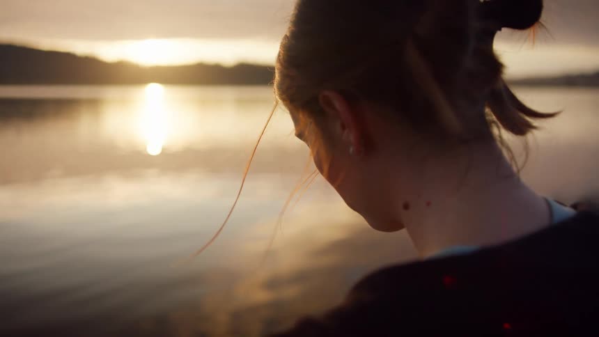 Woman earrings and a zip hoodie reads a book on the shore at dusk