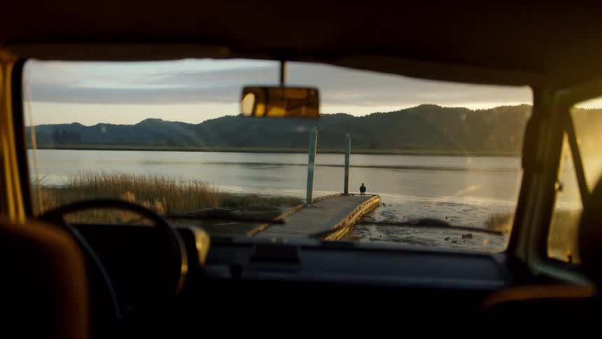 The view from inside a car of a person on a dock looking out at the water