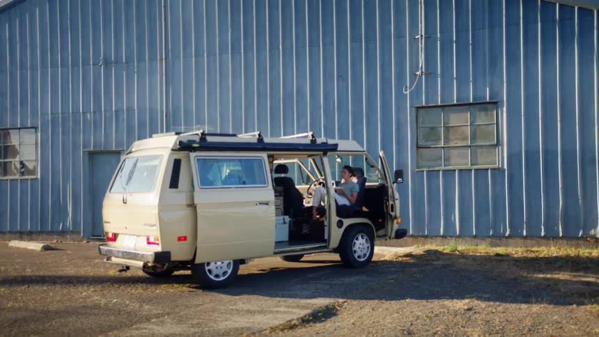 Woman relaxes in van with open doors parked near warehouse