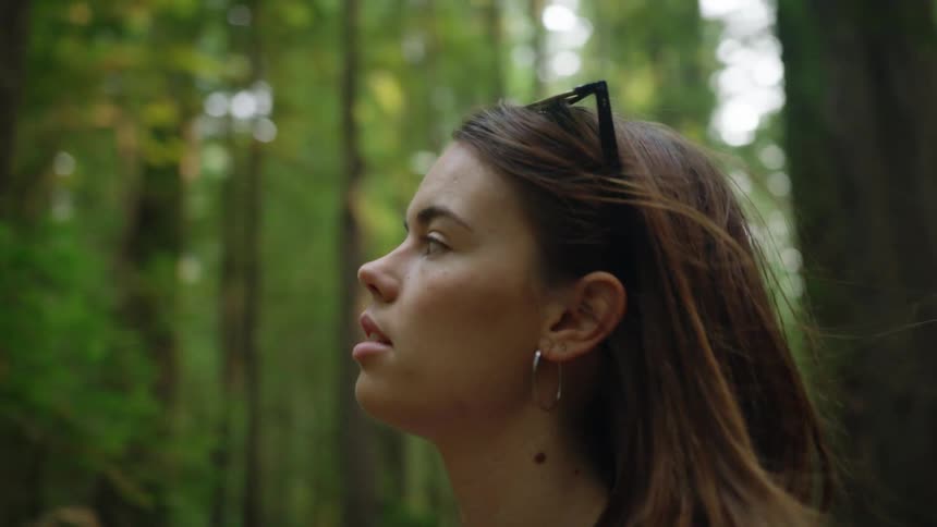 Woman with hoop earrings glasses and a sweatshirt walks in the woods