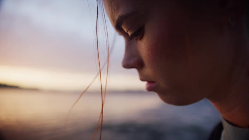 Woman earrings and a zip hoodie reads a book on the shore at dusk