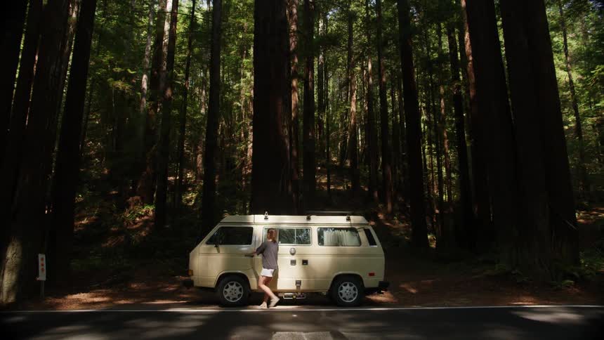 A woman walking and entering a vehicle with a forest with trees in the background