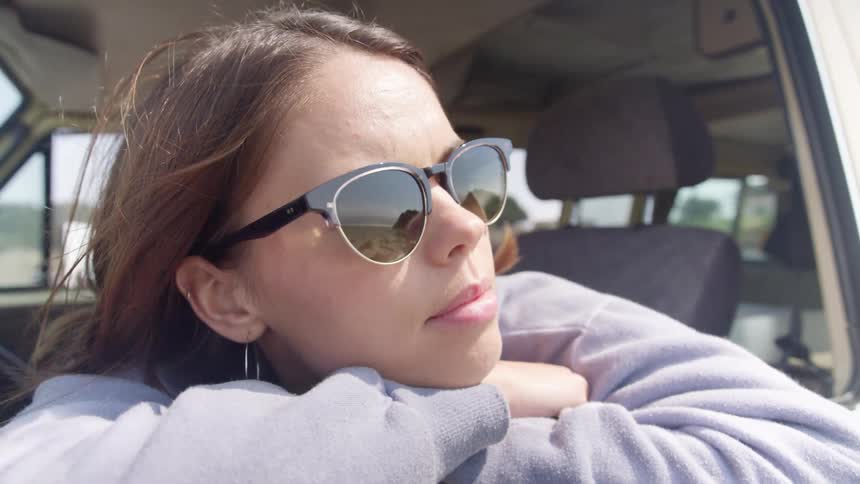 A woman in sunglasses rests in the window of a vehicle during the day