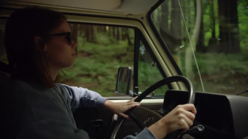 Woman wearing sunglasses drives through forest
