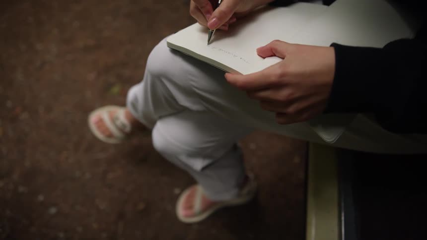 A girl sits outside and writes in a notebook