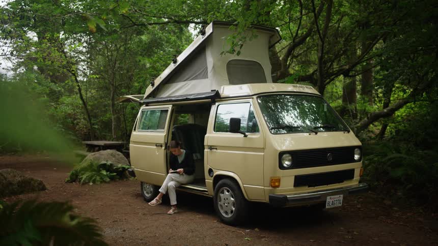 Woman sitting in a camper van with a roof tent in the forest