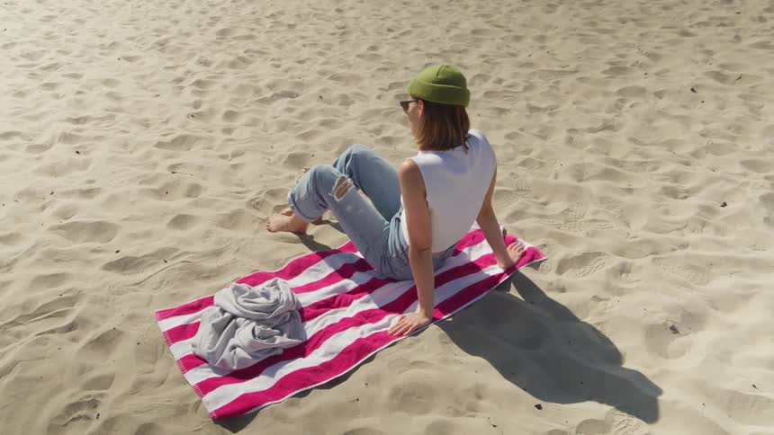A young woman sits on a towel on a beach on a sunny day