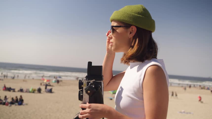A woman stands on the beach and uses a large vintage camera to take photos