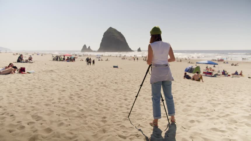 A photographer takes pictures on a beach with people walking and relaxing