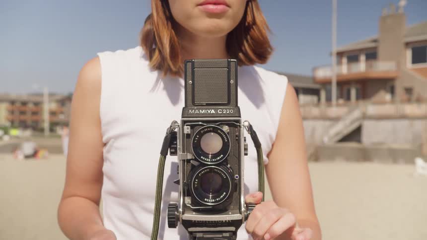 Woman adjusts setting of camera standing on beach near large house