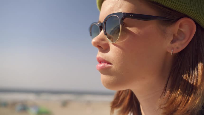 A photographer adjusts her sunglasses while standing at the beach