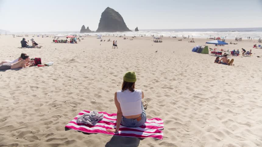 A woman sits on the beach on a blanket looking to the water