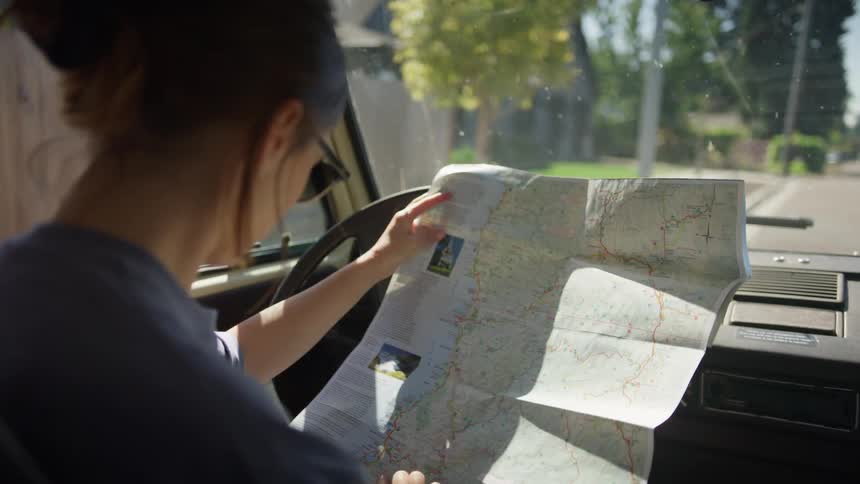 Woman sits in drivers seat of vehicle parked in neighborhood reading map