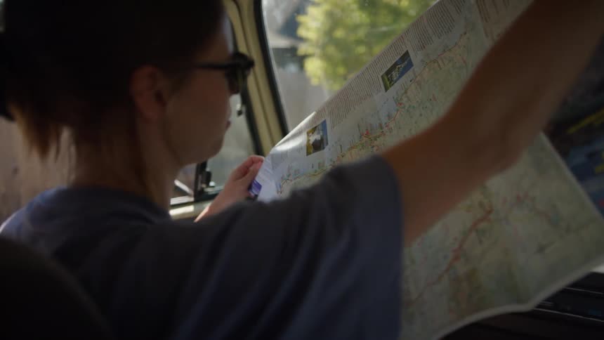 A woman sits in the front seat of a vehicle and opens up a paper map