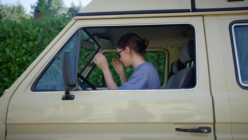 Woman with brown hair and a t shirt wears sunglasses and starts the vehicle