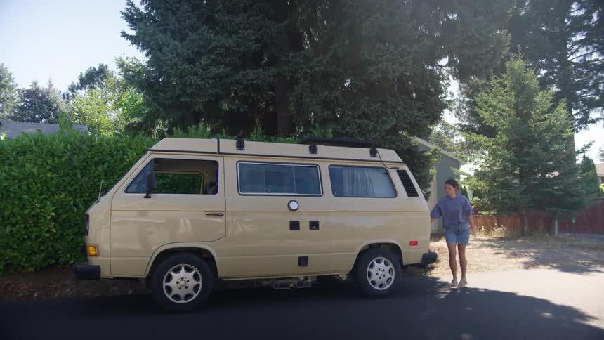 A teenage girl walks away from a house and puts her bag in the back of a van and gets in the drivers seat