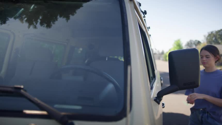 A woman with keys opening a vehicle then going inside with the sky and clouds in the background
