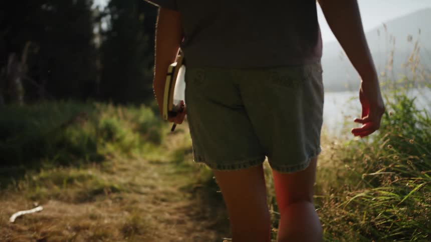 A person with a pen and book walking by a lake with the sky and clouds in the background