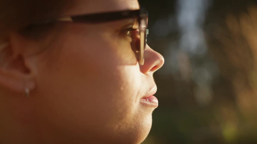 Woman wearing sunglasses faces toward sun shining on her face