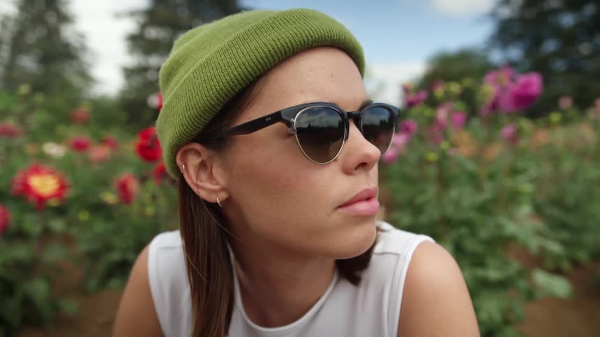 A woman in sunglasses kneels before a row of flowers on a sunny day