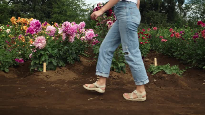 A young woman walks past rows of flowers arranged outdoors during the day