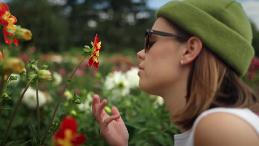 A woman crouches to smell a flower