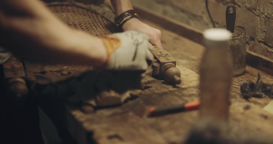 A man in a woodworking shop sands a chair