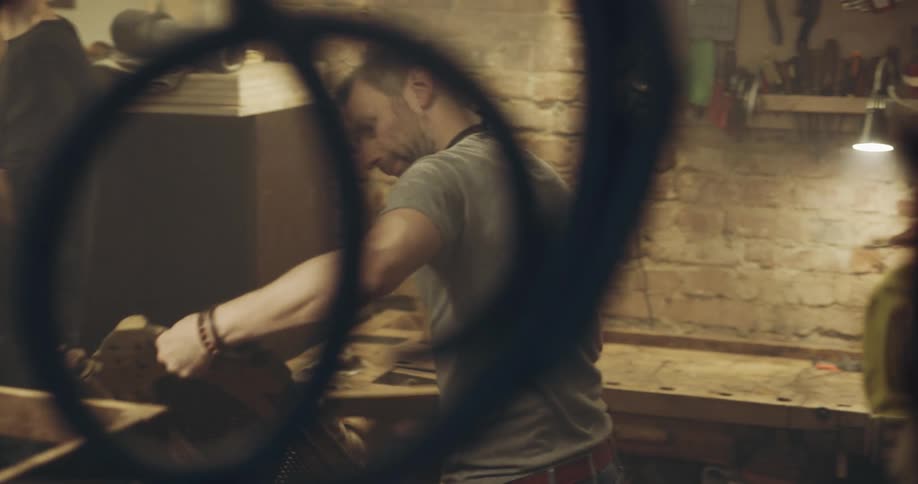 Two men in woodworker shop examine wooden chairs